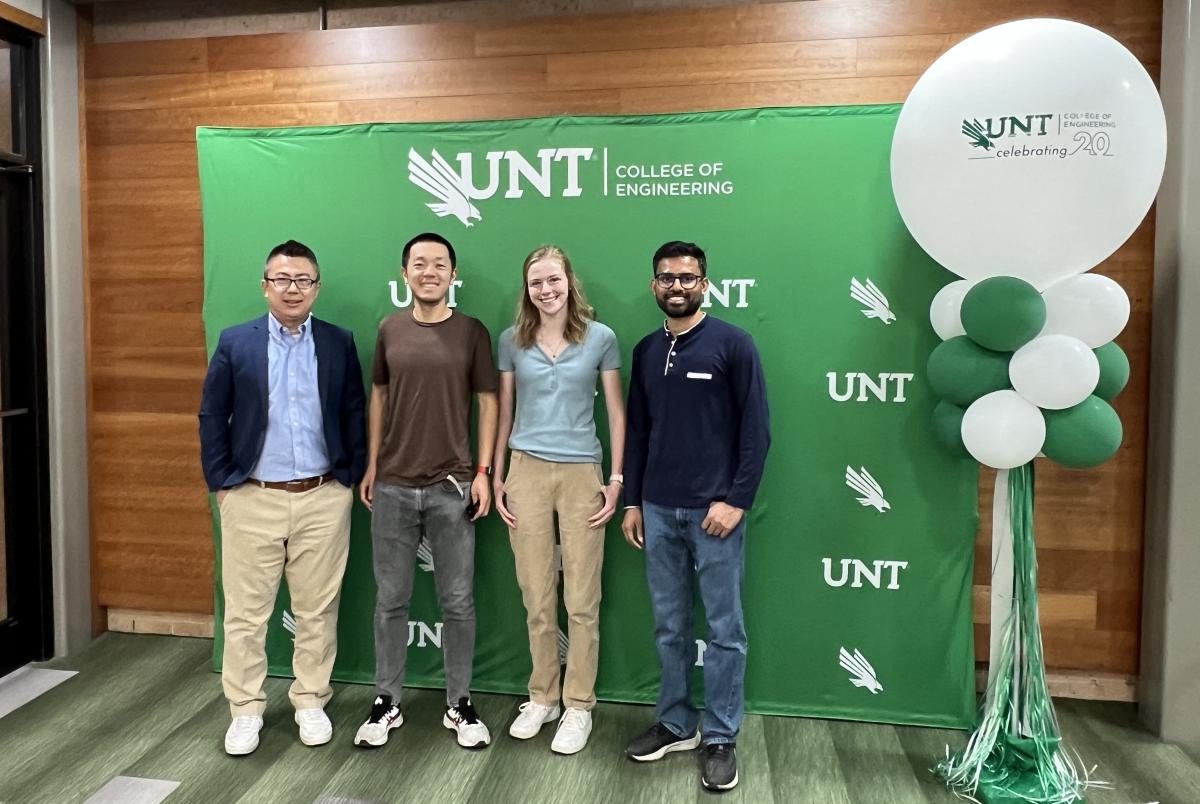Dr. Zheng and three students standing in front of green UNT banner